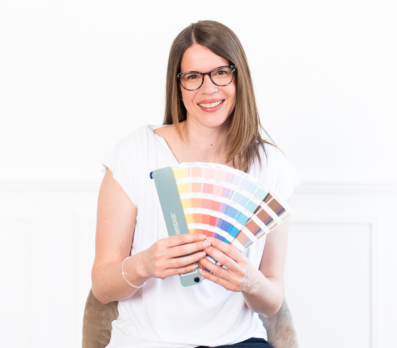 Andrea posing with a fanned open Pantone colour swatch book against a white background wall